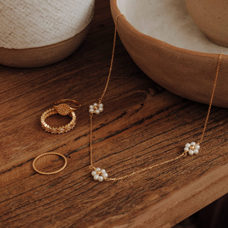Ein Arrangement mit der zarten und floralen Wildflower Halskette, dem mit Zirkoniasteinen besetzten Eternity Zig Zag Ring, dem Siegelring Pinky Shinig Sun Ring und dem zarten, aber dorch strukturierten Pinky Wavy Ring - alles in 18 karat Gold Veredelung.